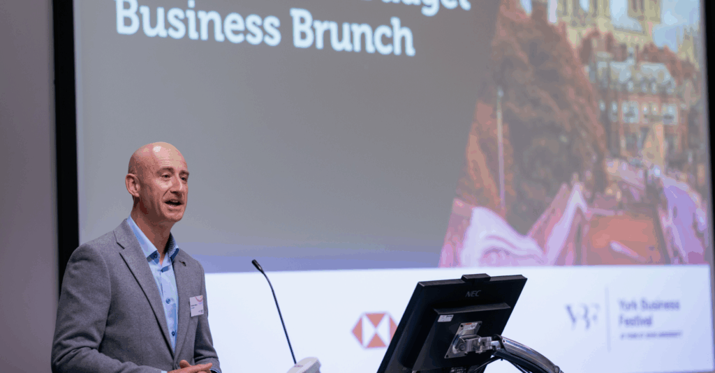 Andrew Lowson stands in front of screen which reads Business Brunch